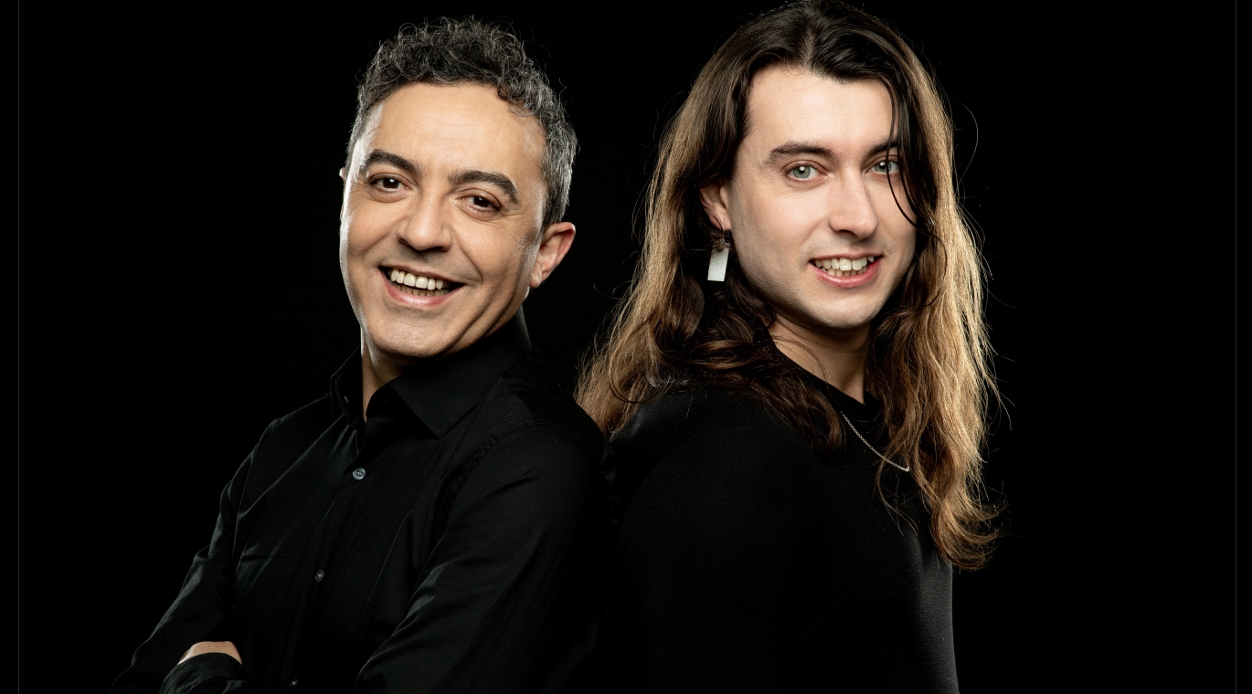 FOTO DE DOS ACTORES DE FRENTE, VESTIDOS DE NEGRO, GESTO SONRIENTE