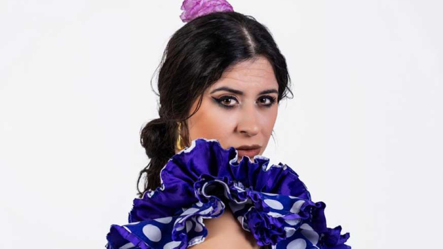 Retrato de una bailaora de flamenco con vestido azul de lunares y volantes, mirando a cámara sobre fondo claro
